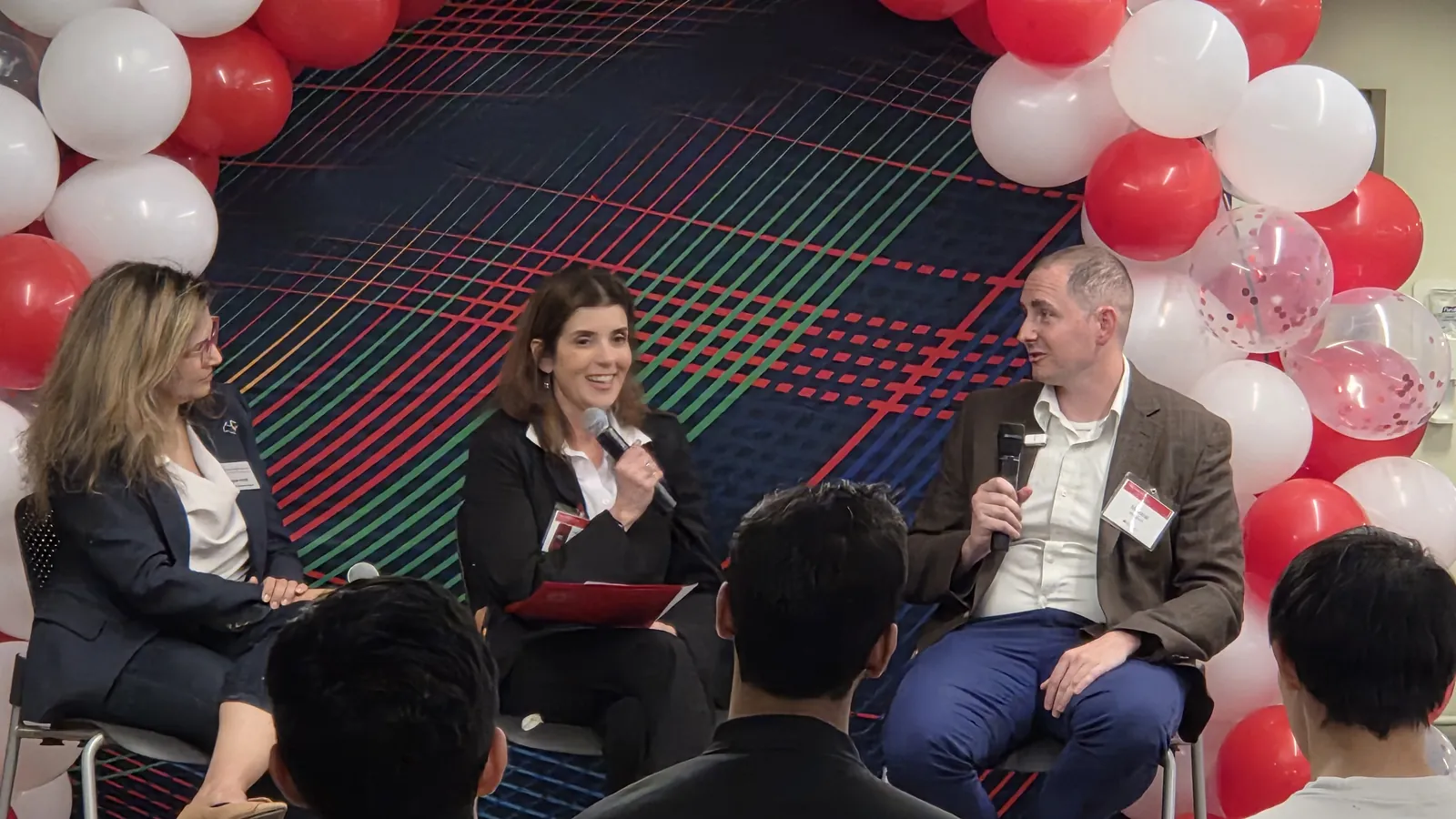 Panelists speak in front of a red and white balloon arch at the CMU INI When AI Attacks panel