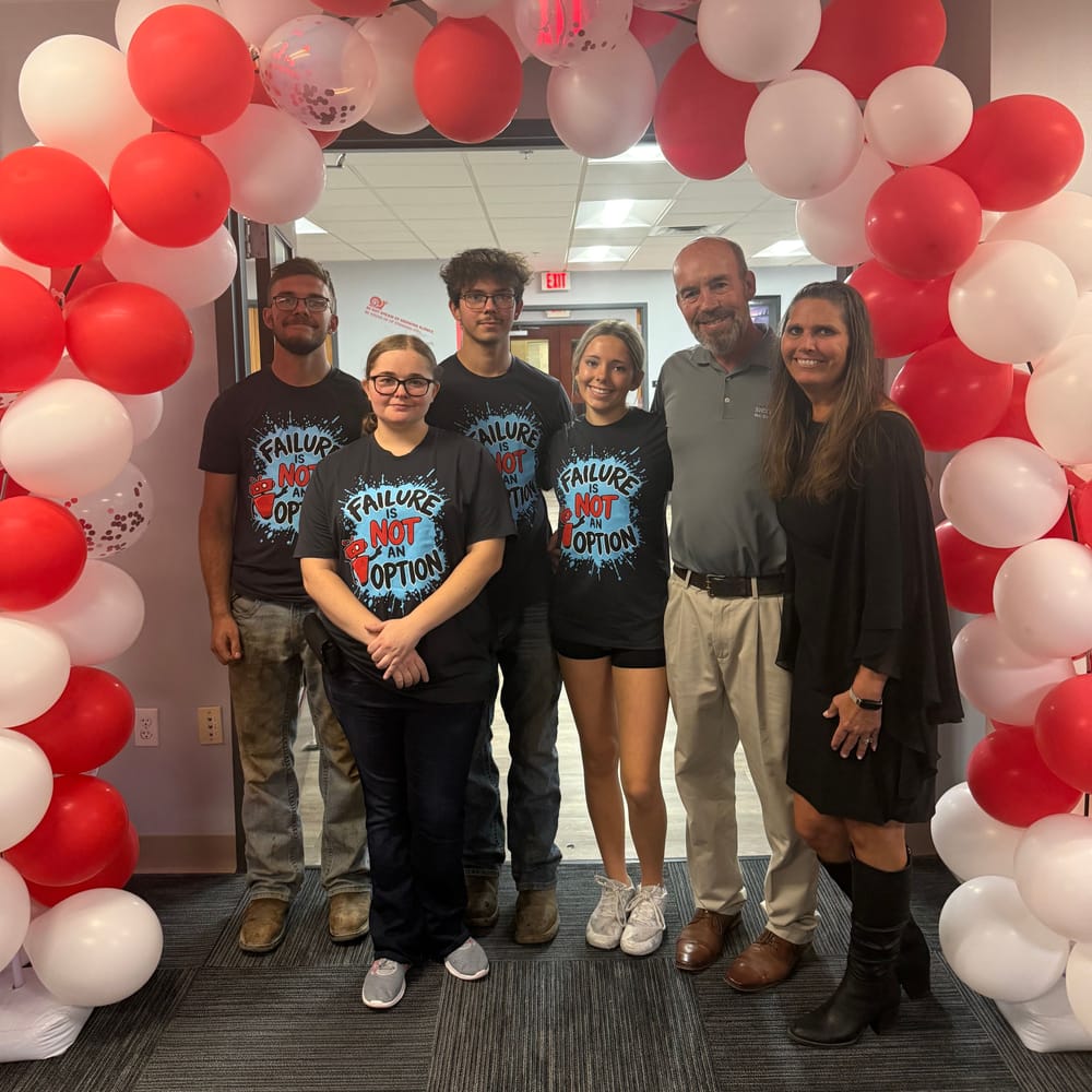 Sierra Experts team members in matching “Failure is not an option” shirts under a red and white balloon arch at the 20th anniversary celebration