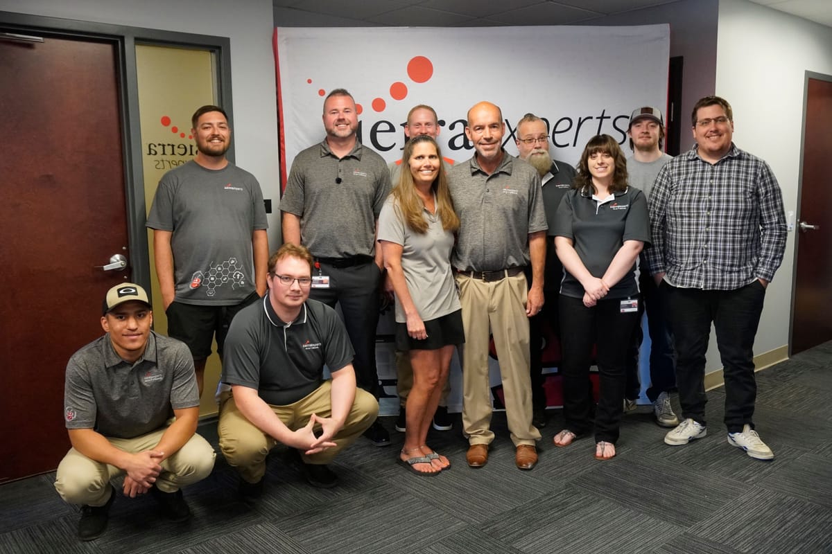 The Sierra Experts team, most in matching Sierra Experts shirts, gathered in front of the company banner at the office
